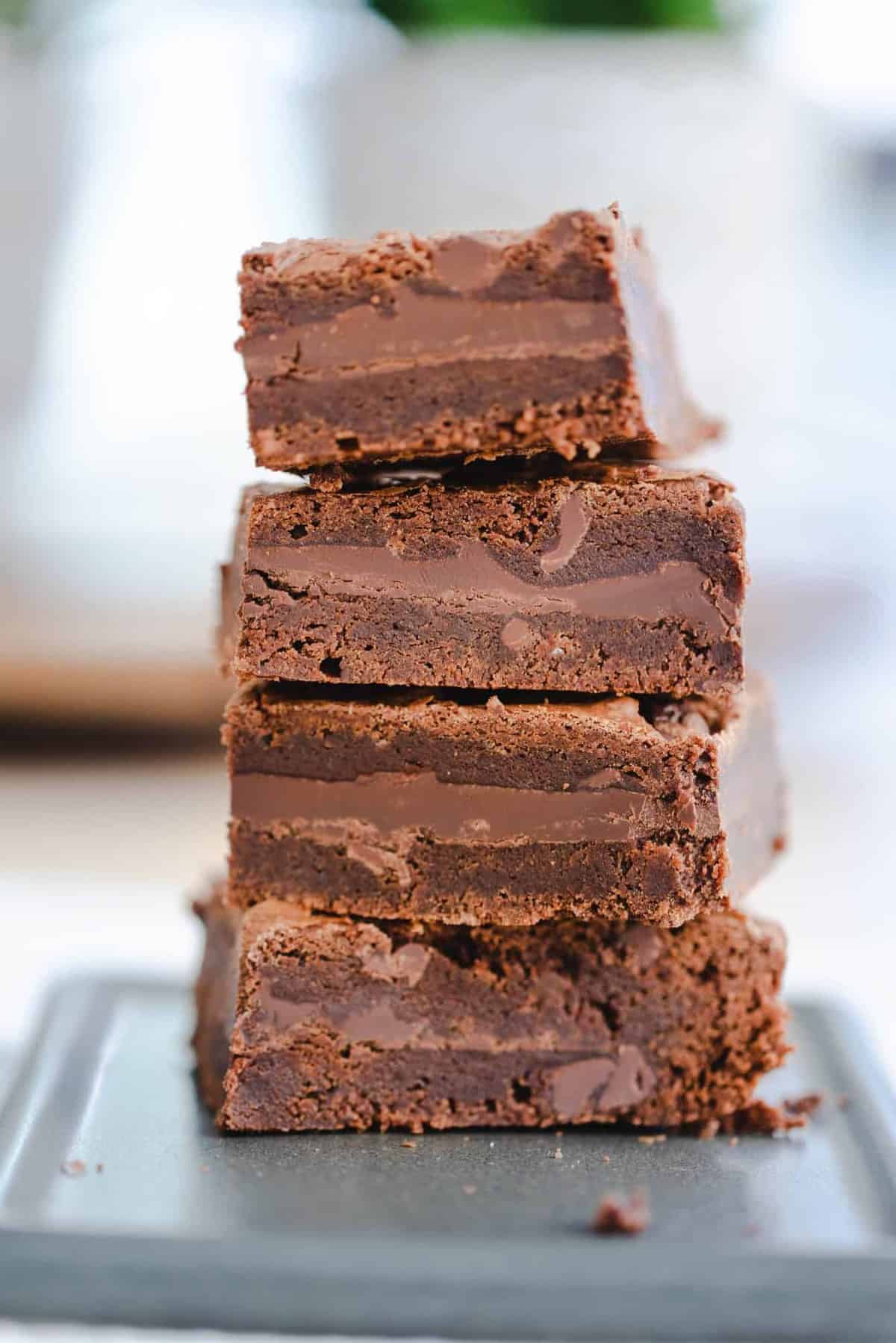 Four brownies are stacked on top of one another. You can see the layers of brownie and smooth chocolate bar in each.