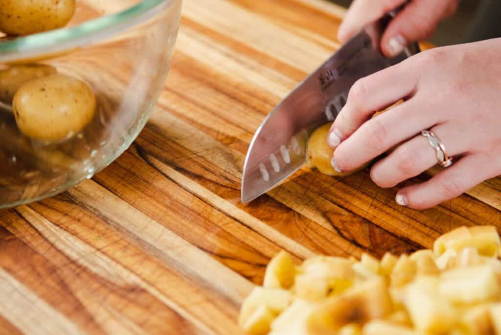 Ashley chops potatoes on a wooden cutting board..