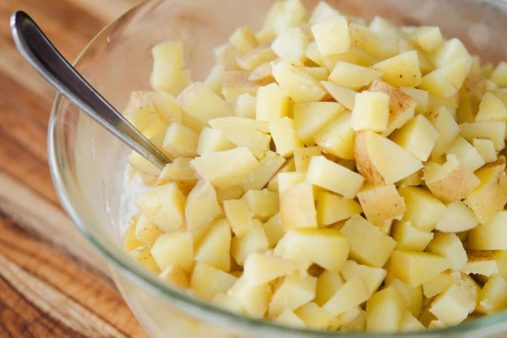 Cooked potatoes sit in a glass mixing bowl on top of the sauce mixture previously prepared.