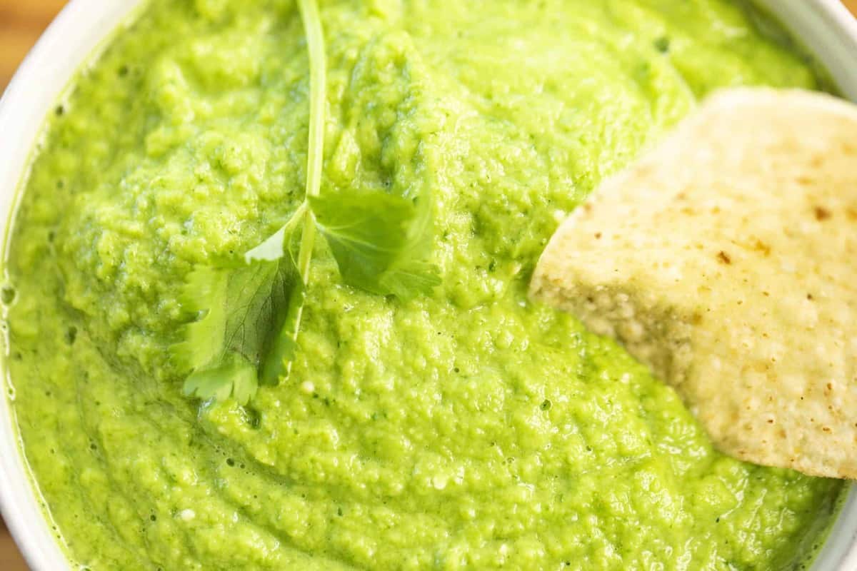 Bright vibrant green salsa sits in a bowl with a fresh tortilla chip.