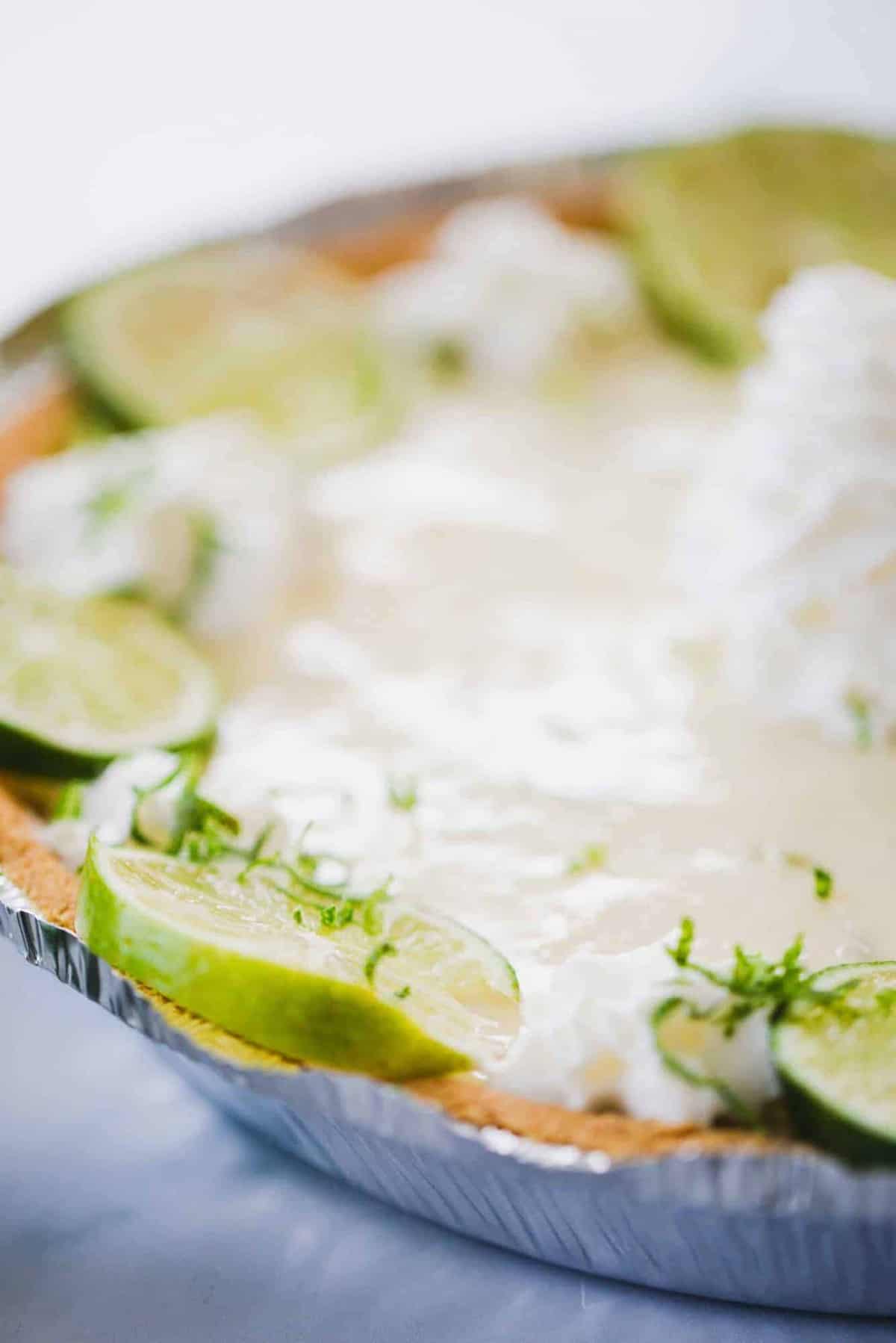 Key Lime Pie sits on a counter, adorned with slices of lime and whipped cream.