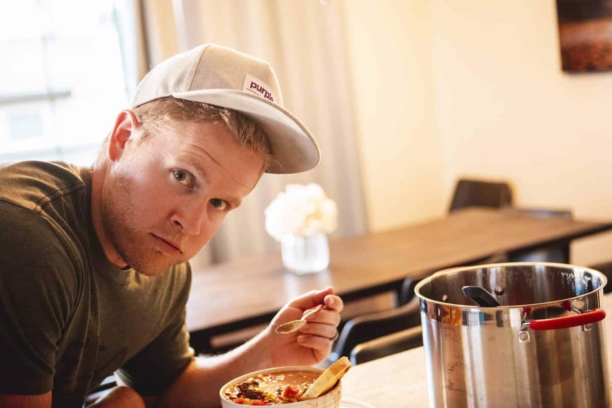Dallin leans over the counter with a bowl of chili, spoon in hand, ready to take a bite.