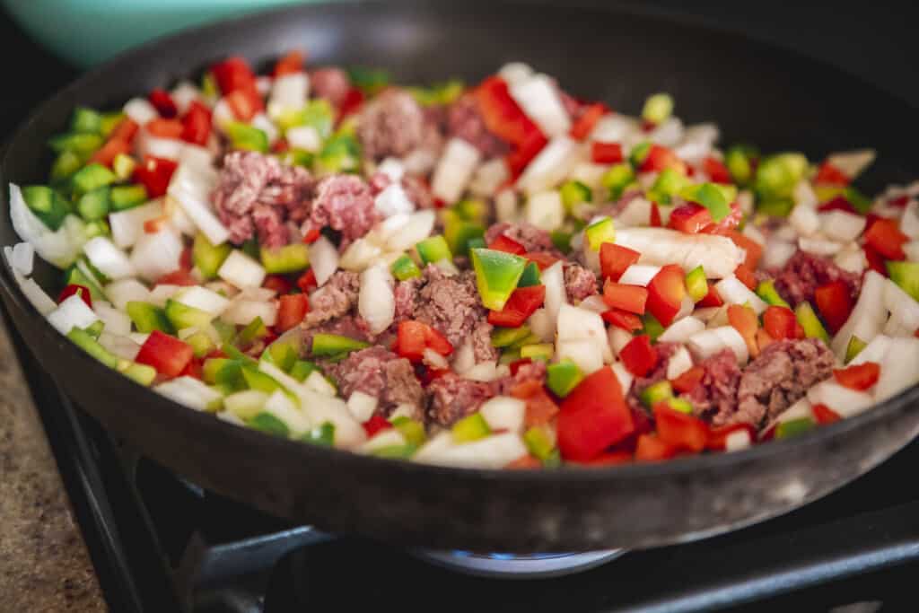 Chopped onions, peppers, ground beef sit in a pan cooking slowly.