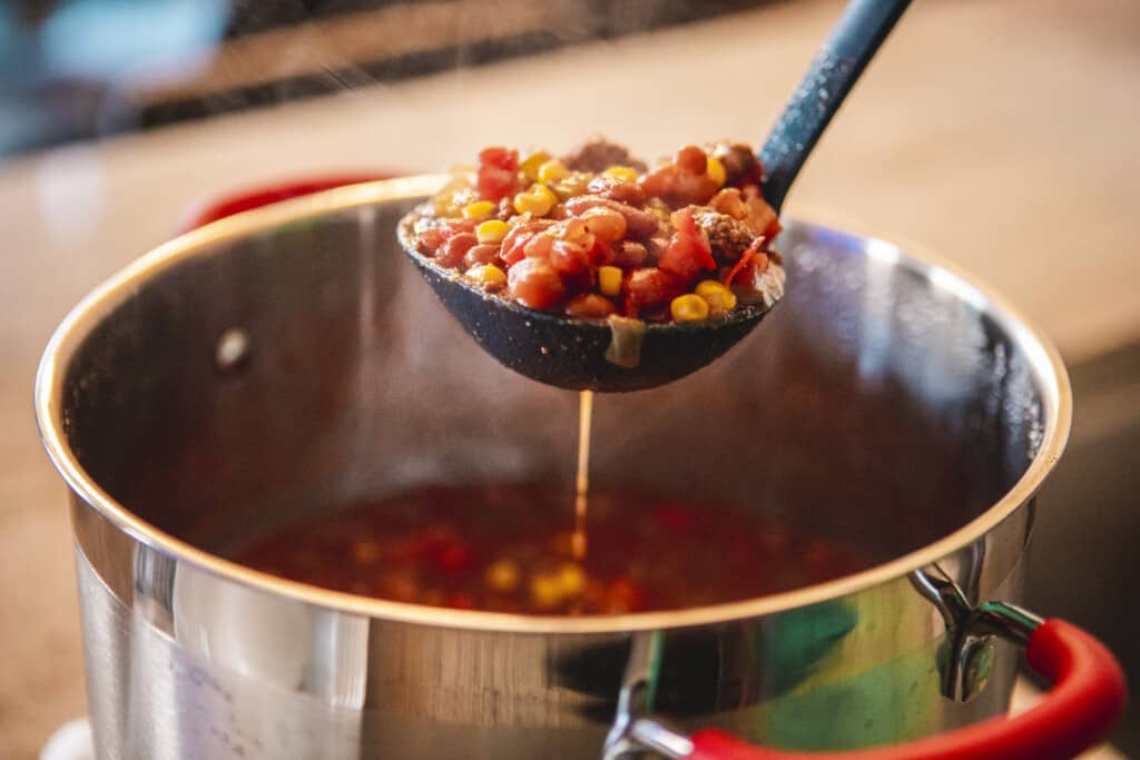 A ladel scoops sweet and spicy chili from a pot.