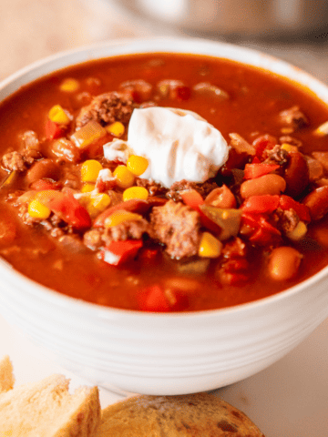 Bowl of Sweet and Spicy Chili sits on a white plate with dollop of sour cream on top.