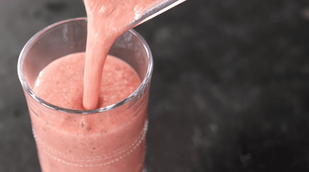 Watermelon Smoothie is being poured from blender into tall glass cup.