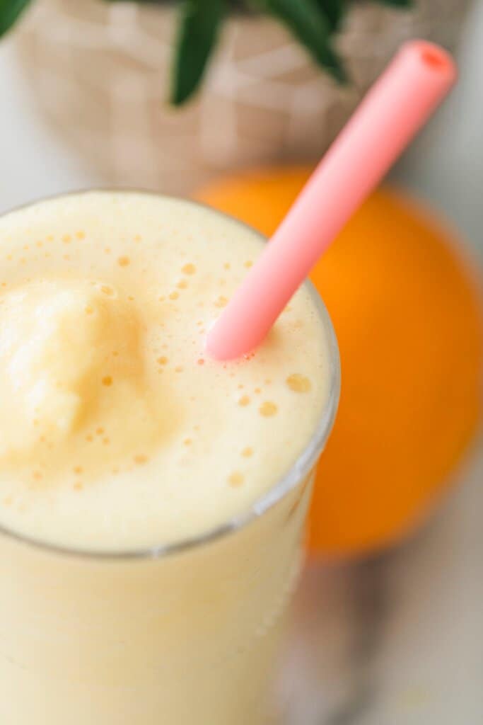 Orange Julius smoothie sits in a tall glass with pink silicone straw inside.