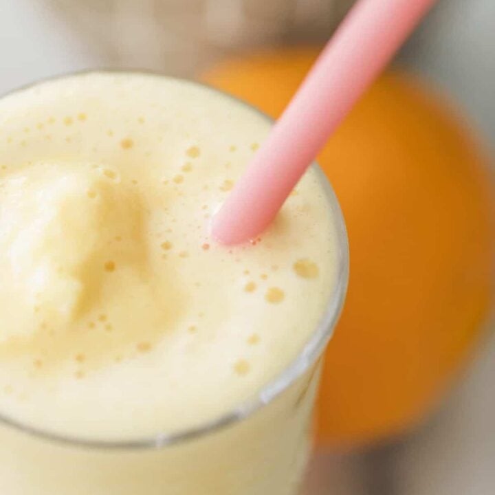 Orange Julius smoothie sits in a tall glass with pink silicone straw inside.