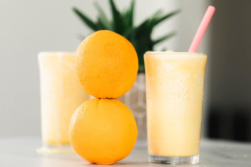 Orange Julius Smoothie in a glass ready to drink. Two oranges stacked on the left of the glass.