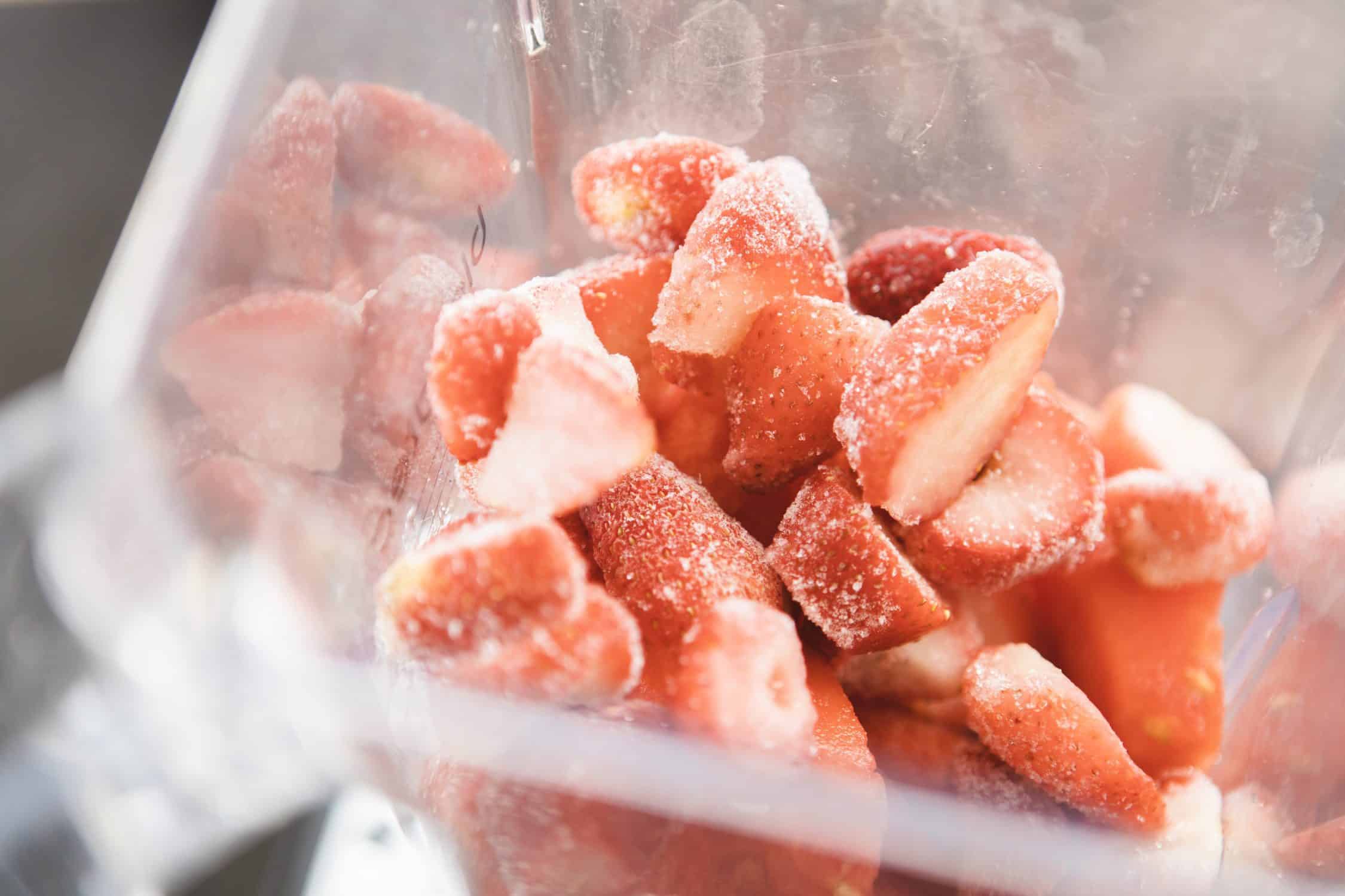 Looking down into the blender cup we see frozen strawberry chunks.