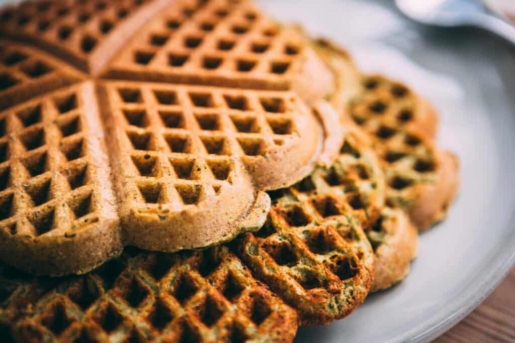 Closeup of three heart shaped green and golden brown smoothie waffles sit on a plate.