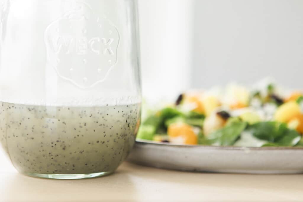 Glass bottle of poppy seed dressing sits to the left of a plate full of citrus salad. 