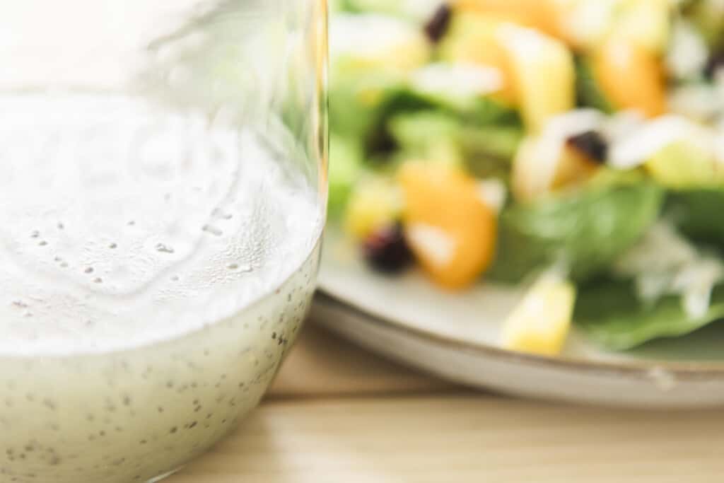 Bottle of fresh made poppy seed dressing sits to the left of a plate of citrus salad.