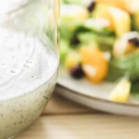 Poppy seed dressing sits in a glass bottle next to a colorful salad on a plate.