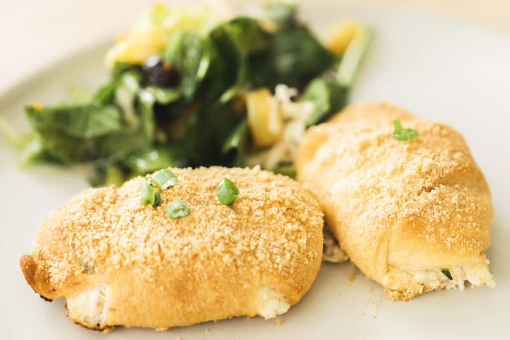 Two Chicken Crescent Roll Ups sit on a plate alongside a fresh salad ready to eat.