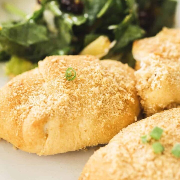 Three Chicken Crescent Roll Ups sit on a plate alongside a fresh salad.