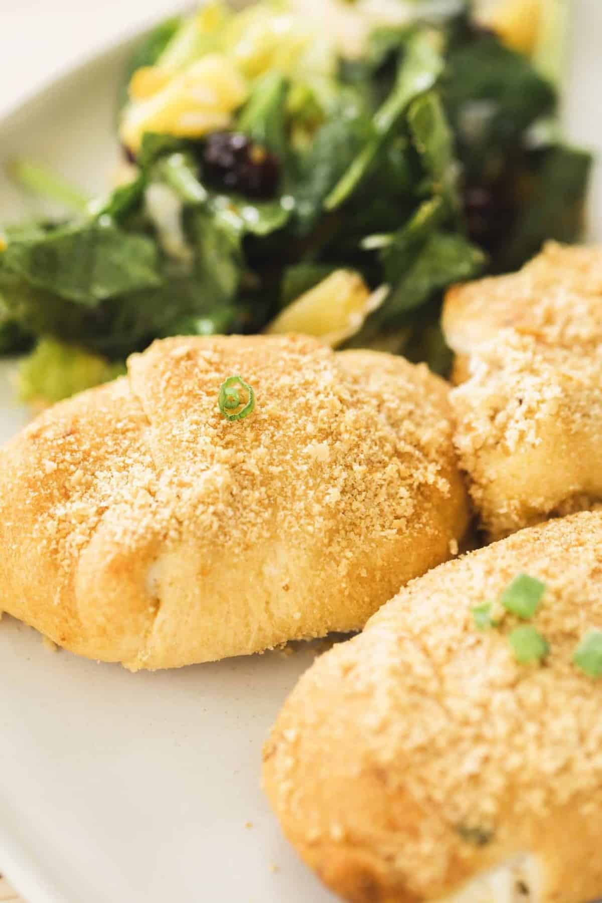 Three Chicken Crescent Roll Ups sit on a plate alongside a fresh salad.