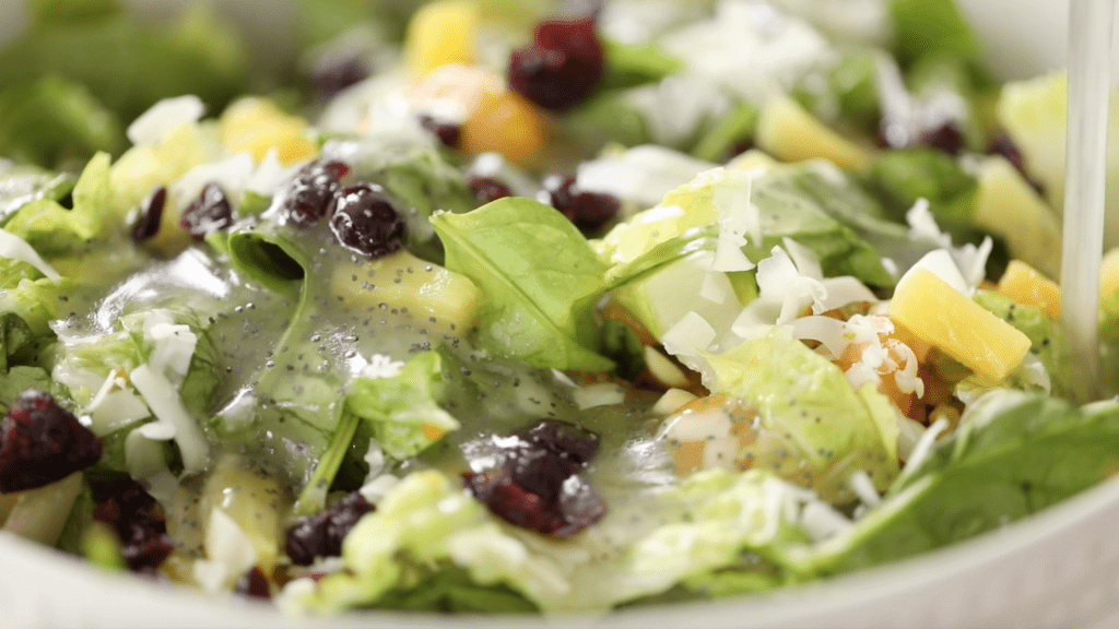 Citrus and cranberry salad sits with freshly poured poppy seed dressing on it.