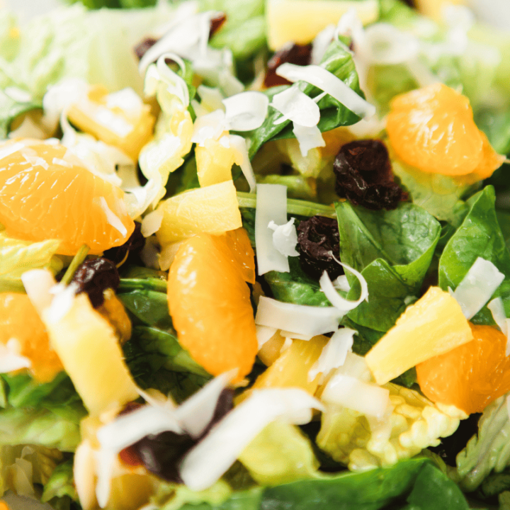 Pineapple, oranges, sliced almonds, swiss cheese, dried cranberries, and romaine sit on a serving plate.
