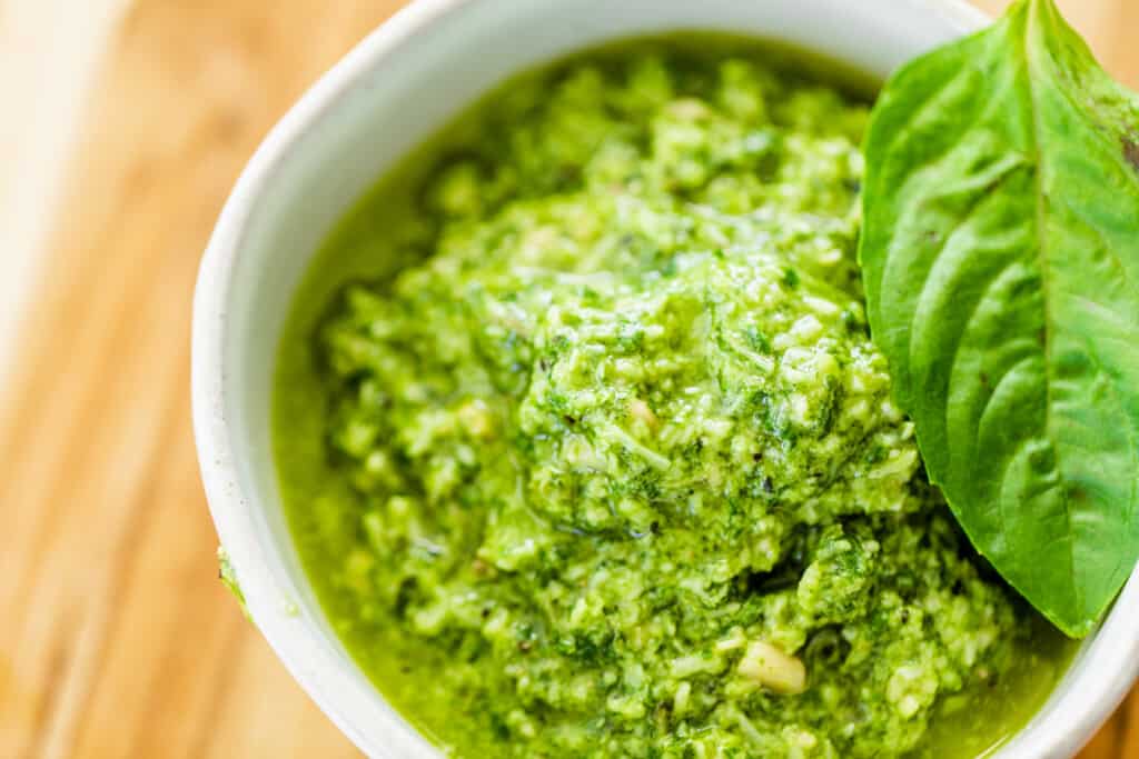 Bowl full of freshly made pesto sauce topped with a basil leaf. 