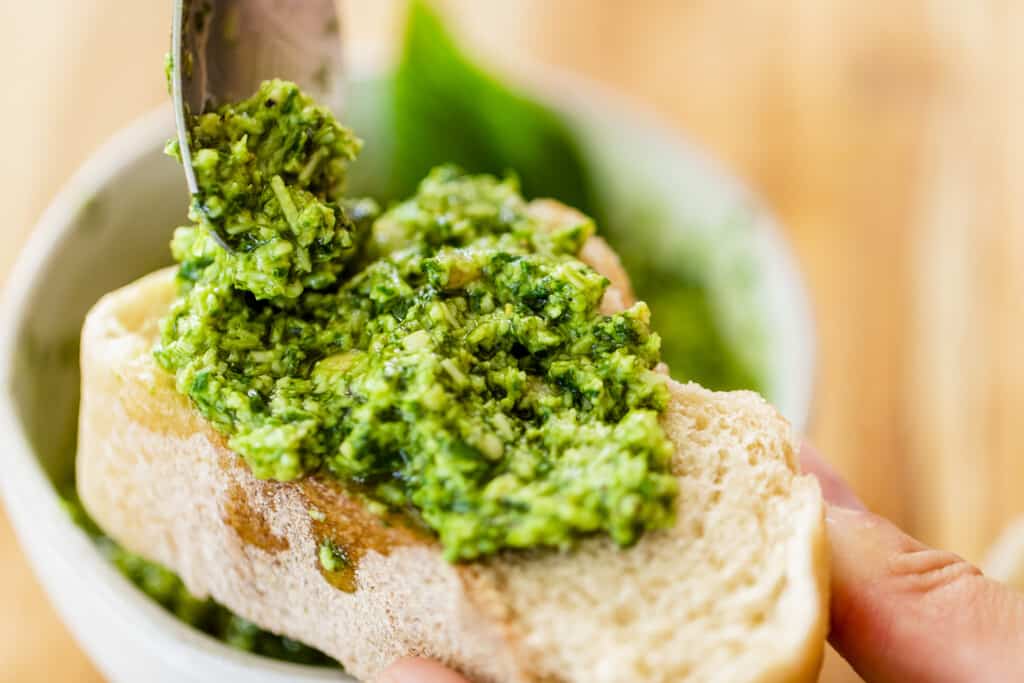 Freshly made pesto sauce is being spooned onto a thick slice of bread. 