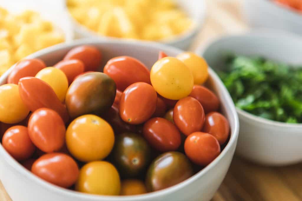 In a bowl sits ripened cherry tomatoes, red, dark greens and yellows. 