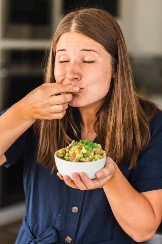 Ashley stands eating a bite of this mango avocado salsa on a tortilla chip. With eyes closed she enjoys its sweet, tangy flavor. 