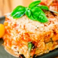Slice of zucchini and pesto lasagna sits on a plate ready to eat. It is garnished with fresh basil leaves.