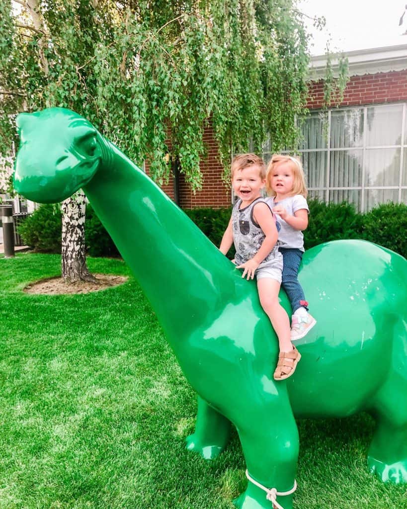 George and James sit on the back of a large green dinosaur.