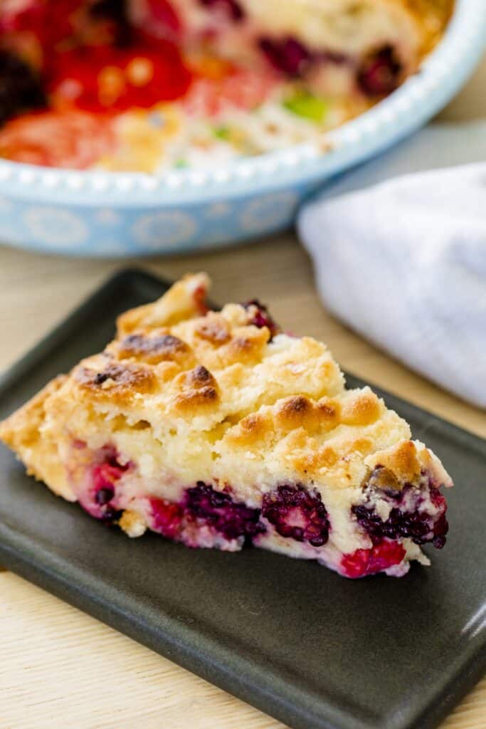 A slice of Double Berry Custard pie sits on a plate ready to be eaten. The pie dish sits behind the plate.