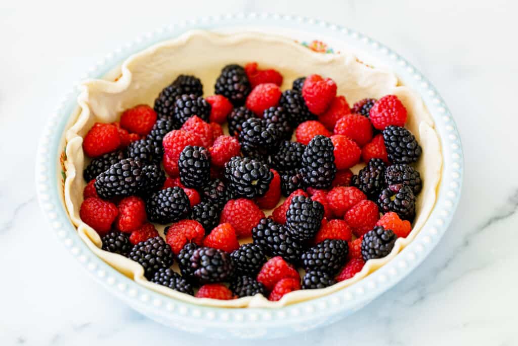 A simple light blue pie tin is lined with a pie crust and filled with vibrant mixed raspberries and blackberries.