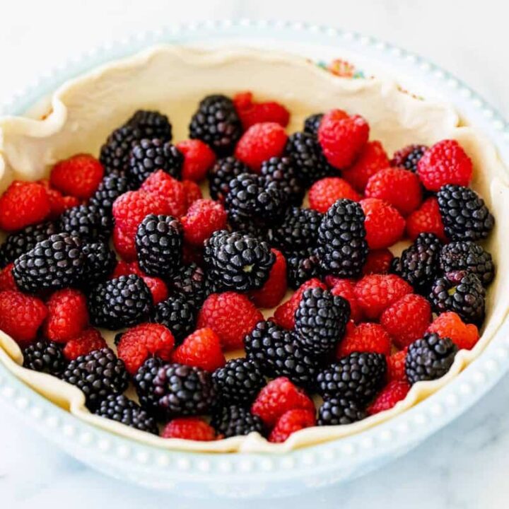A simple egg blue pie tin is lined with a pie crust and filled with vibrant mixed raspberries and blackberries.