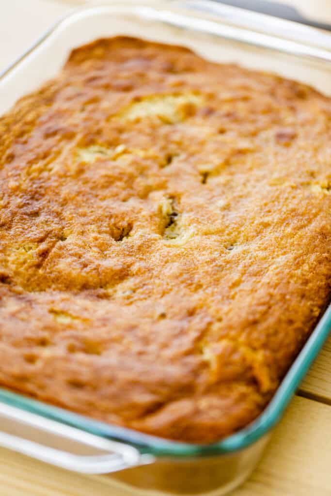 Fresh banana cake sits in a glass 9x13 dish, un-iced and golden brown.