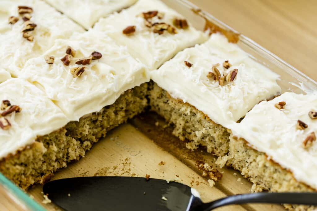 Fresh Banana Cake garnished with Coconut Cream Cheese frosting, shredded coconut and pecans, sits in a 9x13 dish.