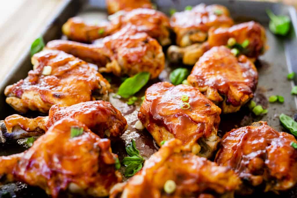 Juicy barbecue chicken sits on a pan. Thighs and drumsticks are generously coated with barbecue sauce.