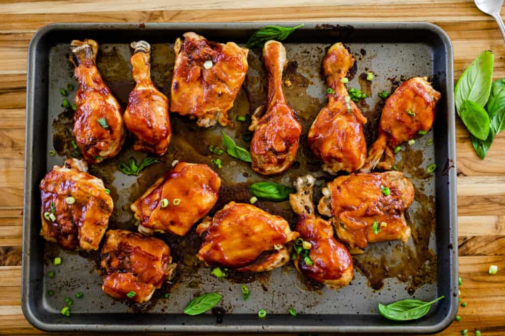 Delicious drumsticks and thighs sit on a baking sheet covered in caramelized barbecue sauce, ready to enjoy.