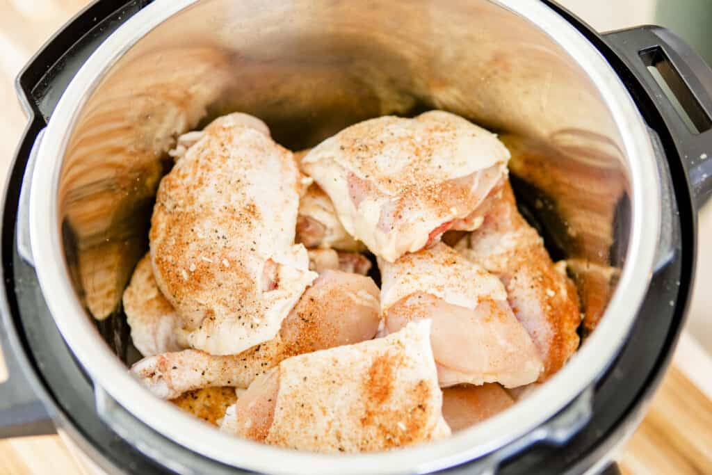 Pieces of chicken are stacked on top of one another inside the Instant Pot ready to be cooked.