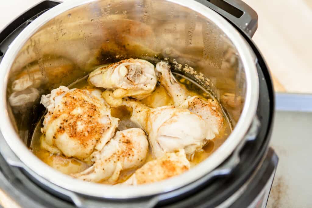 Fully cooked chicken thighs and drumsticks sit in chicken stock inside the Instant Pot. 