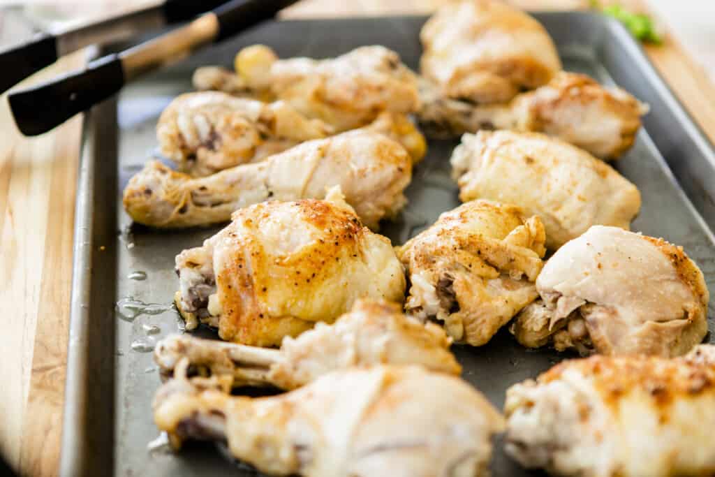 Fully cooked chicken thighs and drumsticks sit on a 13x9 pan cooling and waiting for the next step in the process.