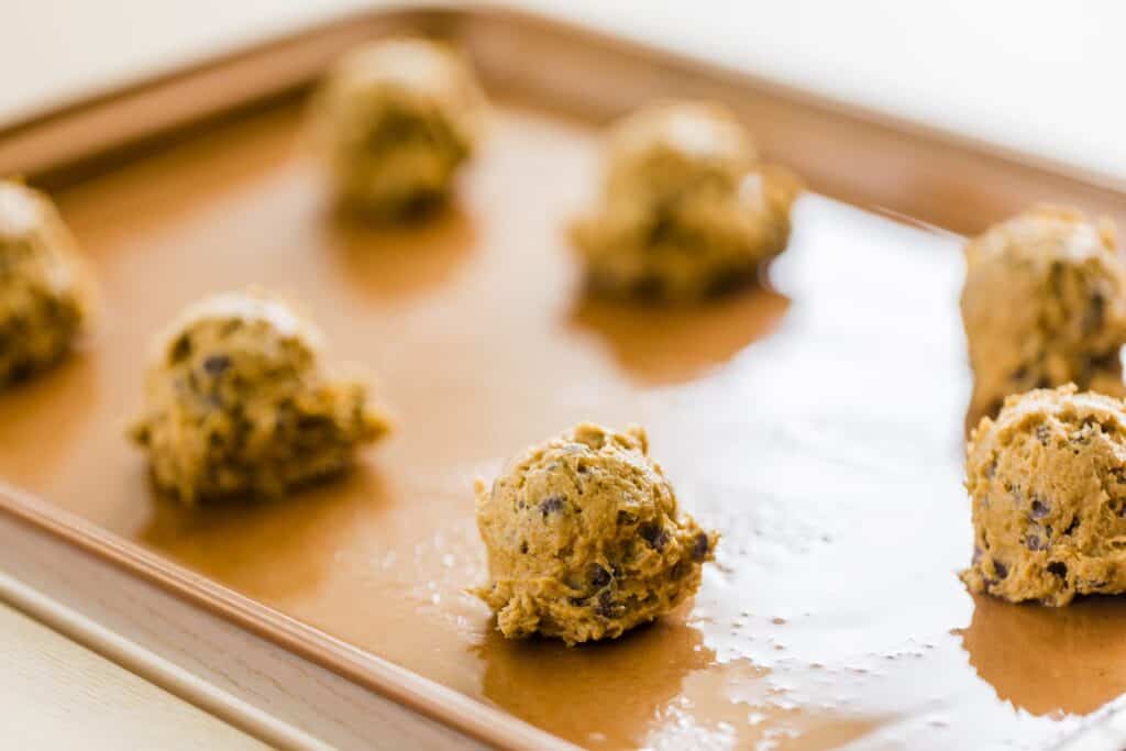Scooped balls of cookie dough are sitting on a greased cookie sheet.