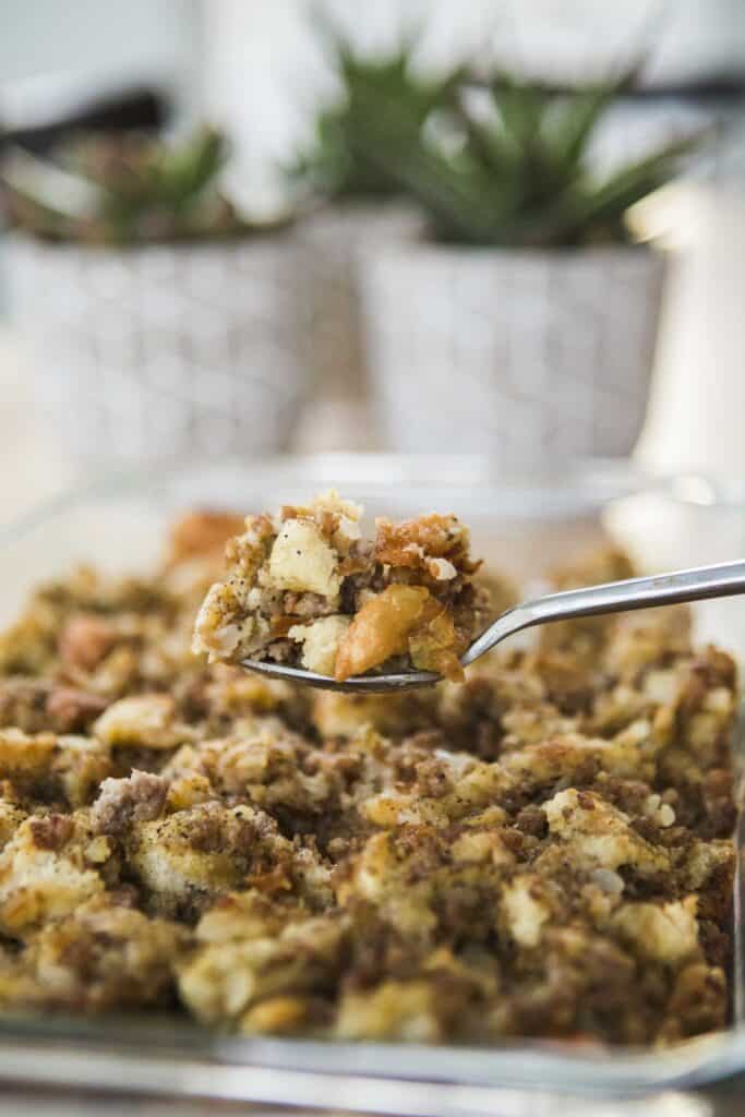 Spoonful of hearty sausage stuffing sits over a baked casserole dish.