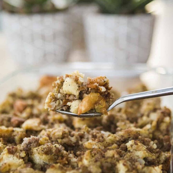 Spoonful of hearty sausage stuffing sits over a baked casserole dish.