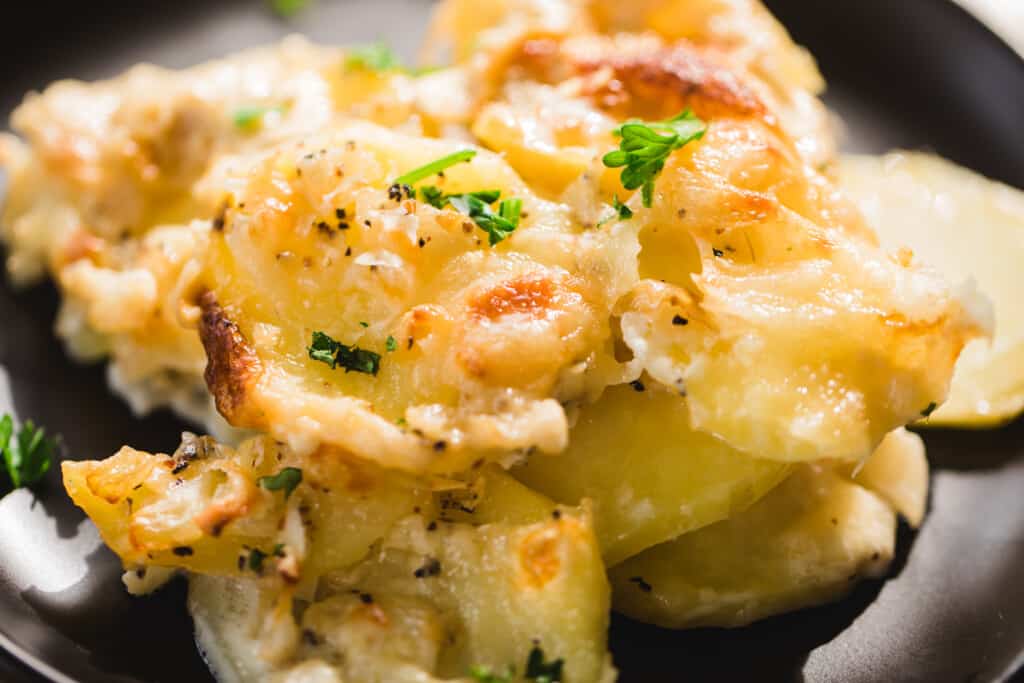 A serving of easy cheesy potatoes Au Gratin sits on a plate. Hot, ready to eat.