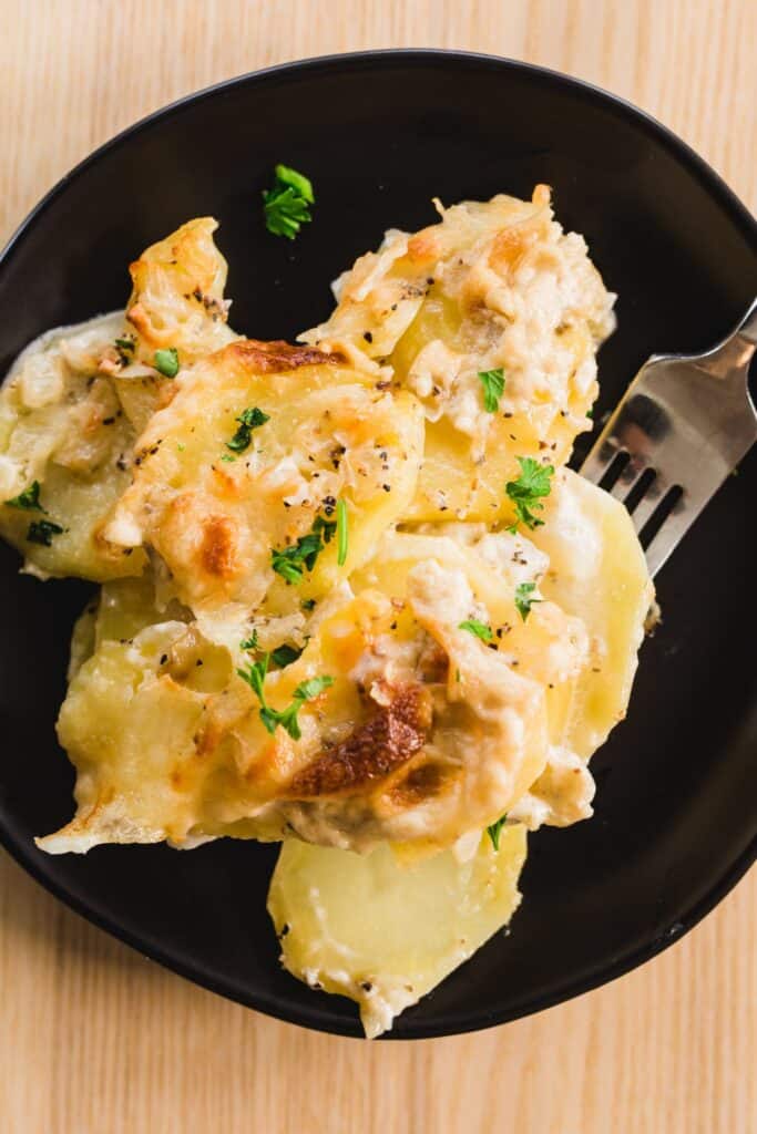 A serving of potatoes Au Gratin sits on a plate. Hot, ready to eat.