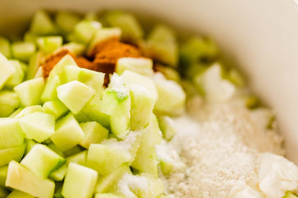 Cut apple slices sit in a bowl with other ingredients for he filling waiting to be mixed.