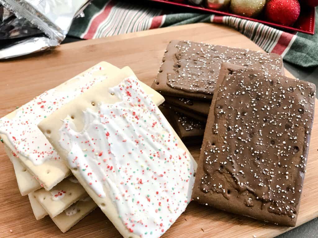 Two stacks of pop tarts, frosted strawberry and chocolate fudge sit on a board ready to assemble for holiday houses.