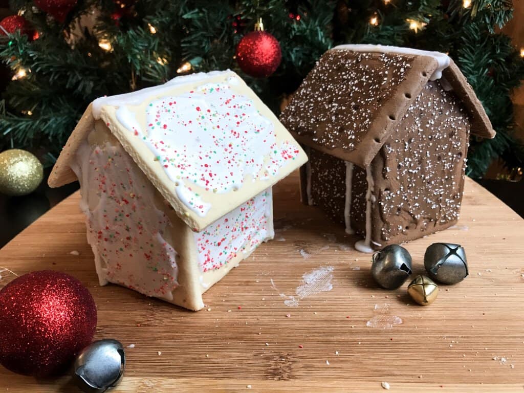 Two pop tart houses sit in front of a lit Christmas tree ready for decorations. Jingle Bells surround the houses.