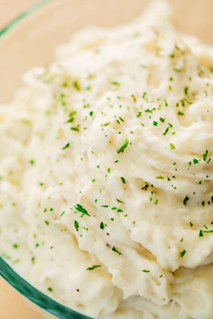 Bowl of fluffy and silky instant pot mashed potatoes is topped with parsley is ready to serve.