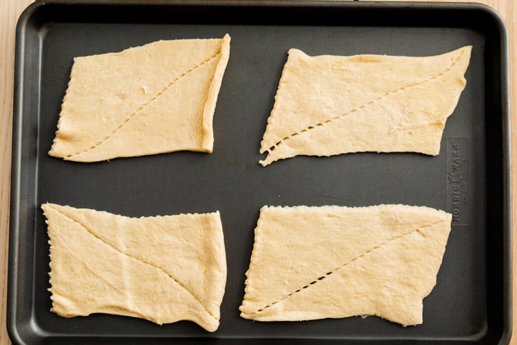 Crescent roll dough has been unrolled and separated into four rectangular sections.