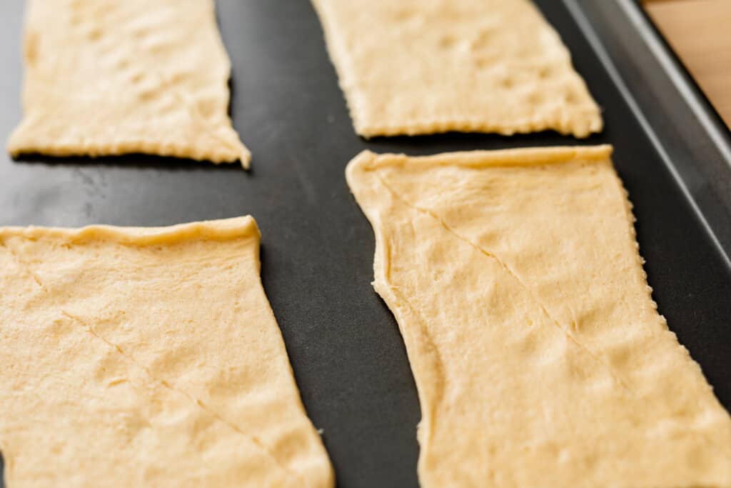 Crescent roll dough has been unrolled into four rectangular sections and the seams of each triangle pinched together.